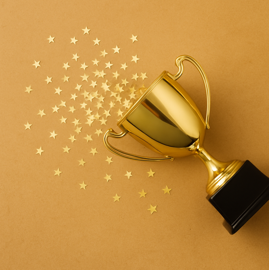 Goldener Siegerpokal liegt seitlich auf braunem Hintergrund, aus ihm fallen zahlreiche kleine goldene Stern-Konfetti heraus.