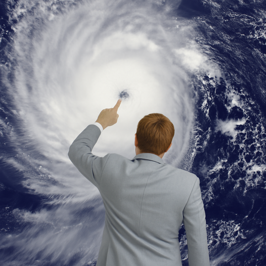 Person im Anzug zeigt mit dem Finger auf das Auge eines großen Wirbelsturms auf einer Wetterkarte oder Satellitenaufnahme.