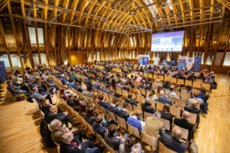 Ein beeindruckender Konferenzsaal mit Holzarchitektur, in dem zahlreiche Teilnehmer einer Präsentation lauschen. Eine große Leinwand zeigt eine Folie mit Windkraftanlagen und dem Titel „The Highlights of the World Energy Outlook 2022“. Die Veranstaltung ist gut besucht, mit Reihen von Zuhörern in formeller Kleidung, die aufmerksam der Diskussion folgen.