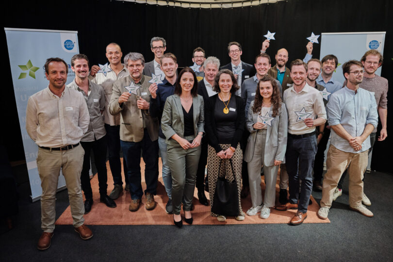 Eine Gruppe von Gewinnern posiert bei einer Preisverleihung, einige halten Stern-Trophäen in den Händen, vor einem Hintergrund mit Bannern des Klimafonds.