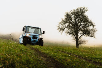Blaues Nutzfahrzeug auf einem Feldweg und Nebel im Hintergrund.