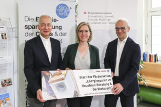 Eine Gruppe von drei Personen, die ein Schild halten, auf dem steht: 'Start der Förderaktion Energiesparen im Haushalt: Beratung & Geräteaustausch'. Im Hintergrund Banner des Klimafonds und des Bundesministeriums für Klimaschutz.