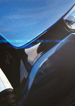 Ein Elektroauto in Nahaufnahme, das gerade an einer Ladestation geladen wird. Der Ladestecker ist angeschlossen, und ein blaues Licht mit einer Ladeanzeige ist sichtbar, was den Ladevorgang symbolisiert.