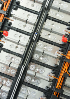 Detailaufnahme eines modularen Batteriesystems mit mehreren Zellen, die durch orangefarbene Kabel und schwarze Halterungen verbunden sind. Die Struktur zeigt eine präzise Anordnung und ist typisch für Energiespeichersysteme, wie sie in Elektrofahrzeugen oder Stromspeichern verwendet werden.