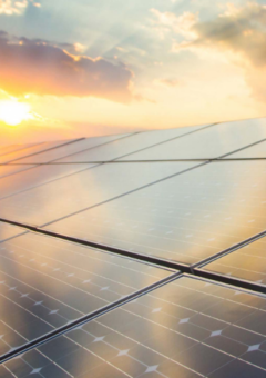 Eine Reihe von Solarmodulen, die das Licht eines Sonnenuntergangs reflektieren. Der Himmel ist von warmen Farben und vereinzelten Wolken geprägt, was die nachhaltige Nutzung von Sonnenenergie betont.