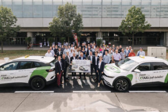 Gruppe von Menschen mit 2 E-Taxis vor modernen Gebäude.