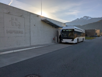 Betonwand mit Relief "H2 MPREIS", im Hintergrund ein stehender weißer FCE-Bus.