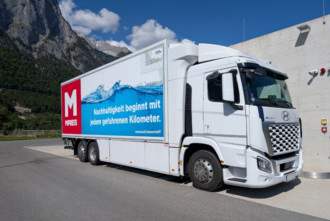Weißer FCE-LKW mit Schriftzug "Nachhaltigkeit beginnt mit jedem gefahrenen Kilometer." vor bergiger Landschaft.