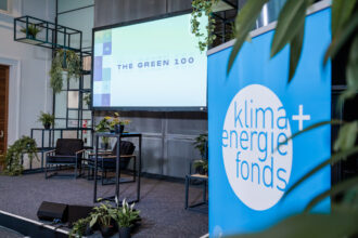 Das Bild zeigt eine Bühne für eine Präsentation oder Podiumsdiskussion mit dem Thema The Green 100. Im Vordergrund steht ein blaues Banner mit dem Logo von 