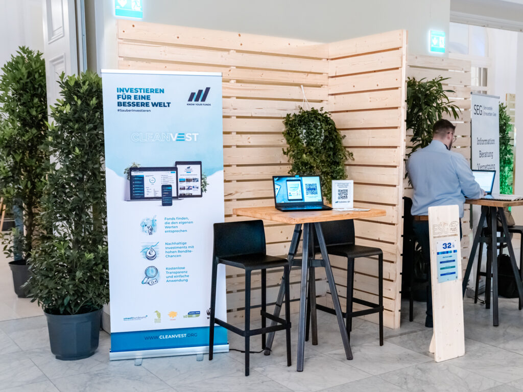 Das Bild zeigt den Messestand von Cleanvest, einer Plattform für nachhaltige Investments. Ein großes, weiß-blaues Banner mit der Aufschrift 