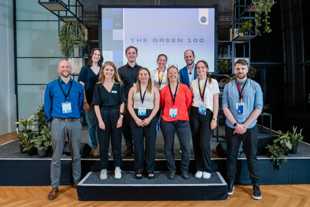 Das Bild zeigt eine Gruppe von zehn Personen, die gemeinsam auf einer Bühne vor einer großen Leinwand mit der Aufschrift 
