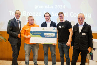 Fünf Männer stehen zusammen auf einer Bühne und lächeln in die Kamera. Drei von ihnen halten gemeinsam einen übergroßen Scheck mit der Aufschrift „TerraBreeze by Social Cooling“ und dem Betrag „EUR 20.000,-“ für die Auszeichnung als „TOP-3 GREENSTART 2024“. Im Hintergrund ist eine Leinwand zu sehen, auf der die Worte „greenstart 2024“ und „TerraBreeze by Social Cooling“ projiziert werden, zusammen mit grafischen Elementen und Pflanzenmotiven. Die Gruppe besteht aus Vertretern des Gewinnerteams und weiteren Beteiligten der Preisverleihung.