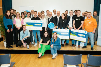 Eine große Gruppe von Menschen steht gemeinsam auf einer Bühne und lächelt in die Kamera. Drei Personen in der ersten Reihe halten übergroße Schecks mit den Aufschriften „sequestra“, „Zukunft Bestand“ und „TerraBreeze by Social Cooling“, jeweils mit dem Betrag „EUR 20.000,-“ und dem Titel „TOP-3 GREENSTART 2024“. Zwei Frauen sitzen vorne auf der Bühnenkante, während der Rest der Gruppe dahinter steht. Links und rechts im Hintergrund befinden sich Roll-up-Banner der „greenstart“-Initiative des Klima- und Energiefonds Österreichs. Die Gruppe besteht aus den Gewinnerinnen, Organisatorinnen und weiteren Beteiligten der Preisverleihung.
