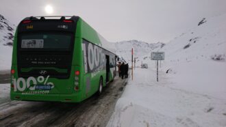 Grüner-weißer mit Wasserstoff betriebener öffentlicher Bus auf beschneiter Straße und Bergen im Hintergrund.