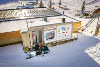 Ein Schneemobil an einer Wasserstofftankstelle in einer verschneiten Landschaft mit Skipisten im Hintergrund.