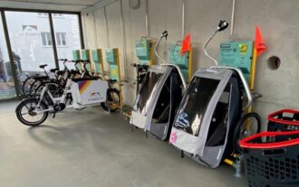 Eine Reihe von geparkten Fahrrädern und Lastenfahrrädern mit Kinderanhängern in einem Gebäude.