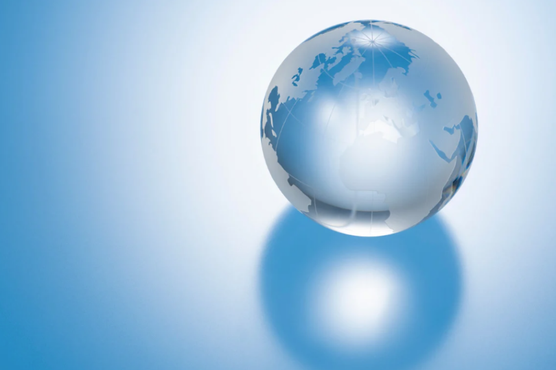 Ein transparenter Globus reflektiert Licht und zeigt Landmassen vor einem sanften blauen Hintergrund, was die globale Verbundenheit symbolisiert.