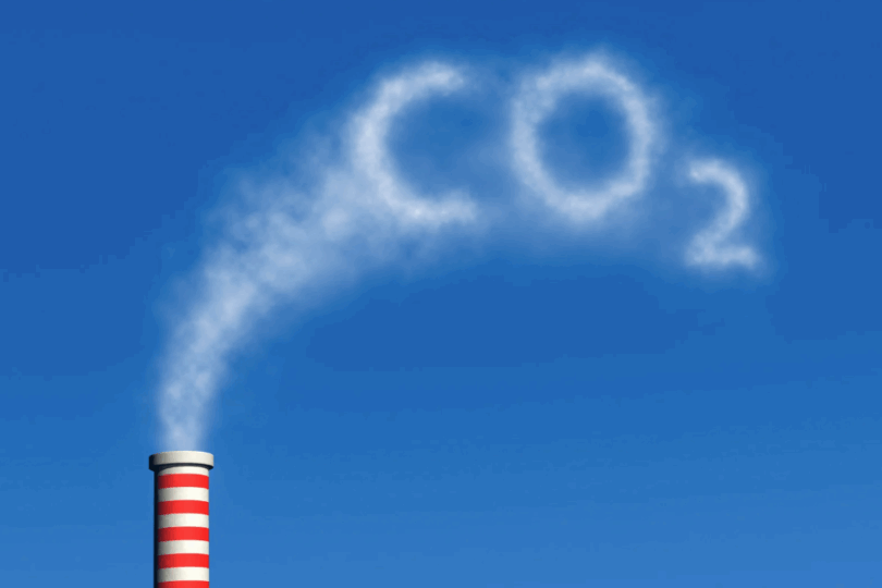 Ein rot-weißer Schornstein strahlt wolkenartige Buchstaben aus, die vor einem strahlend blauen Himmel „CO2“ bilden und die Kohlenstoffemissionen symbolisieren.