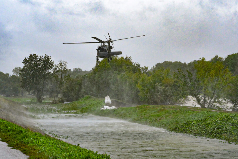 Man sieht einen Helikopter, der während eines Hochwassers Sandsäcke platziert.