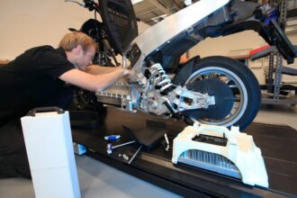 Ein Mechaniker arbeitet am hinteren Teil eines Elektrorollers und konzentriert sich auf die Federung und Motorkomponenten, umgeben von Werkzeugen und Ersatzteilen.