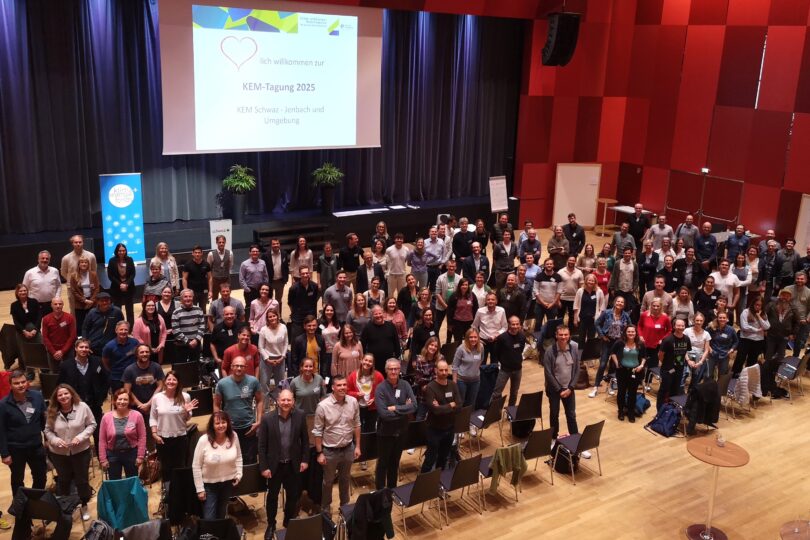 Große Gruppe von Menschen in einem Saal vor einer Bühne mit einer Projektionsleinwand, die 'KEM-Tagung 2025' zeigt