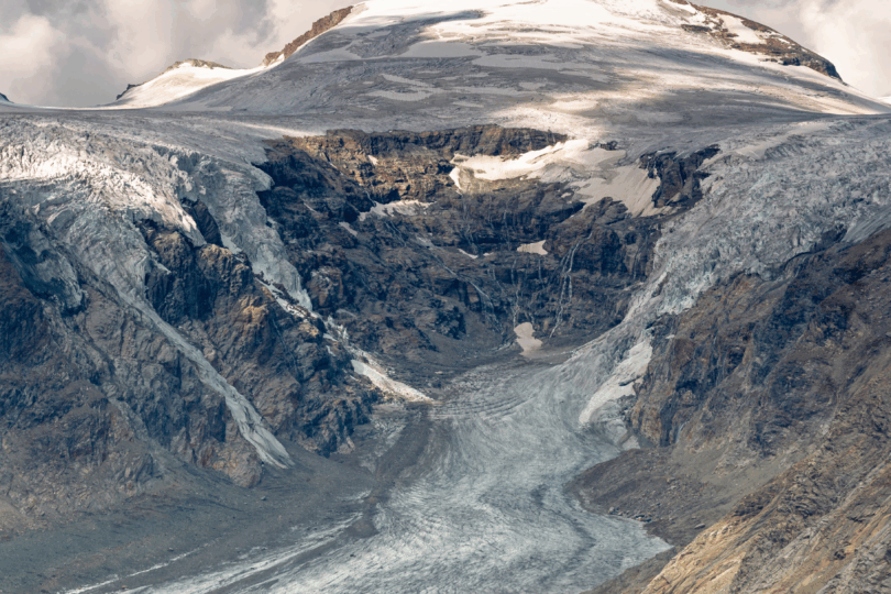 Berg mit Gletscherzunge vor blauem, bewölktem Himmel.