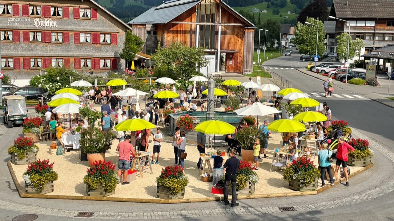 Menschen unter Sonnenschirmen am Dorfplatz