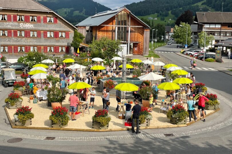 Menschen unter Sonnenschirmen am Dorfplatz