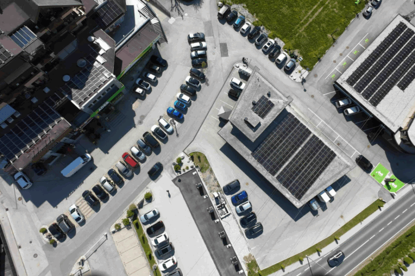 Luftaufnahme eines Parkplatzes mit mehreren Autos neben Gebäuden, die mit Solarpaneelen auf den Dächern ausgestattet sind.