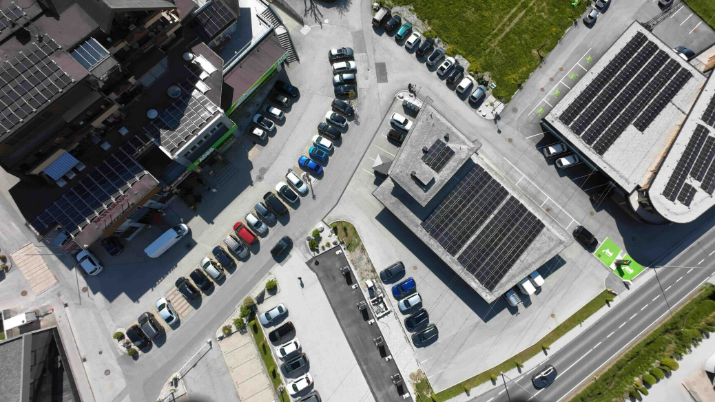 Luftaufnahme eines Parkplatzes mit mehreren Autos neben Gebäuden, die mit Solarpaneelen auf den Dächern ausgestattet sind.