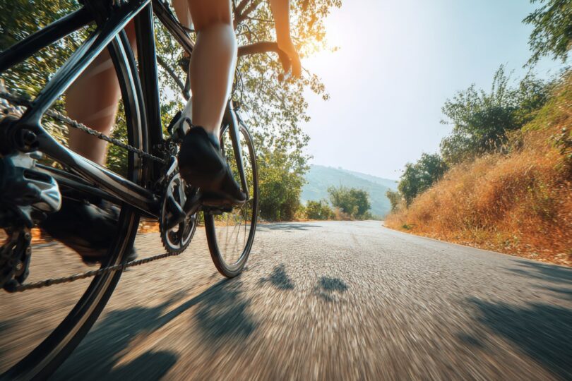 Nahaufnahme von Fahrradfahrern auf einer sonnenbeschienenen Landstraße mit Bäumen und Hügeln im Hintergrund