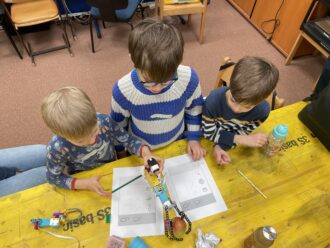 Drei Kinder, die an einem Tisch mit einem elektronischen Greifarm beschäftigt sind.